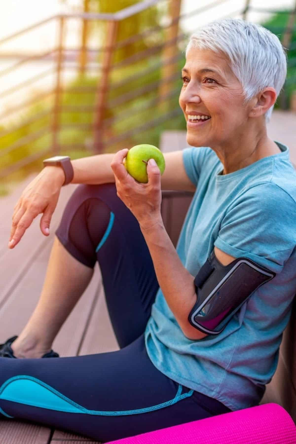 healthy older woman sitting on deck with apple.