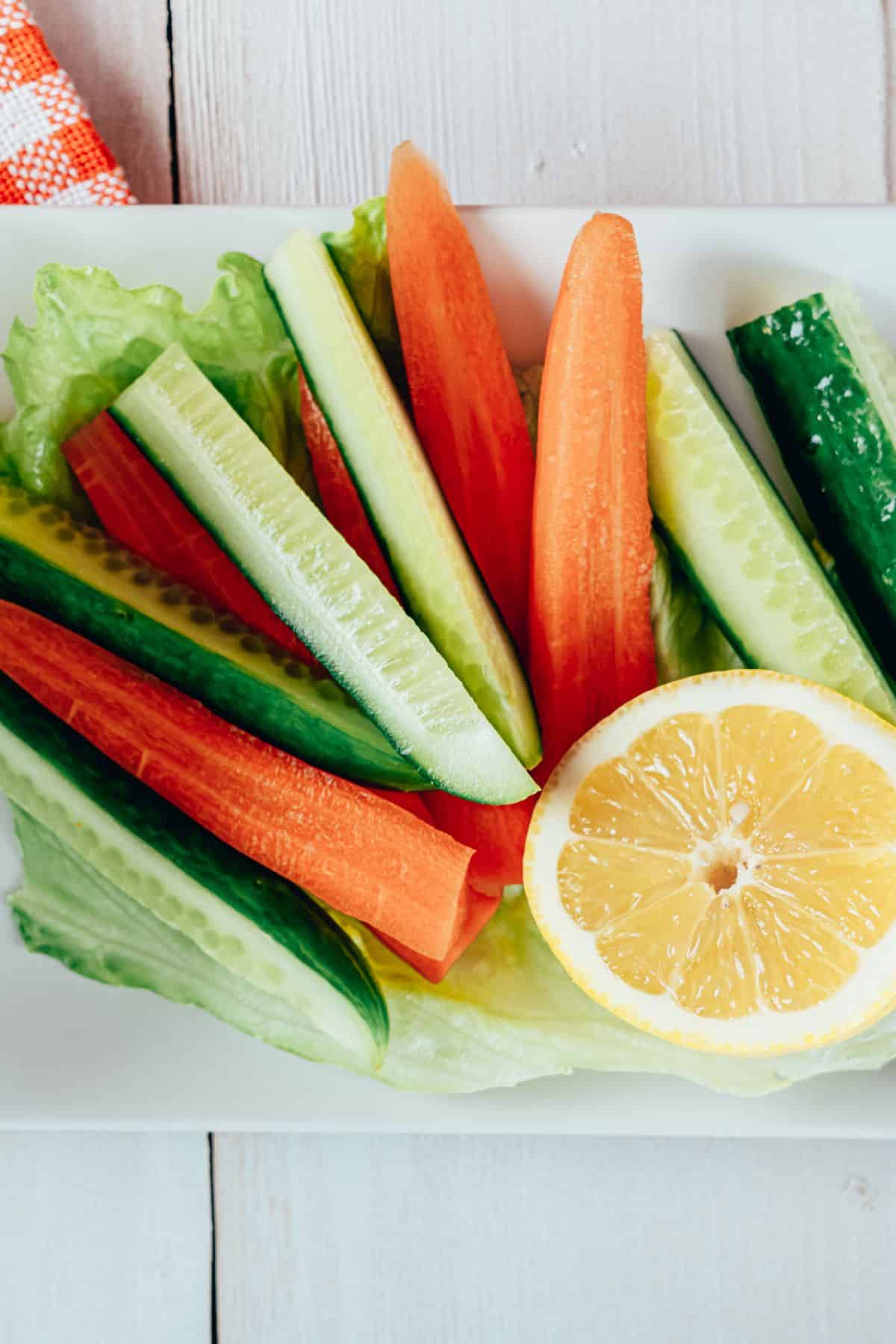 a plate of raw vegetables with a slice of lemon.