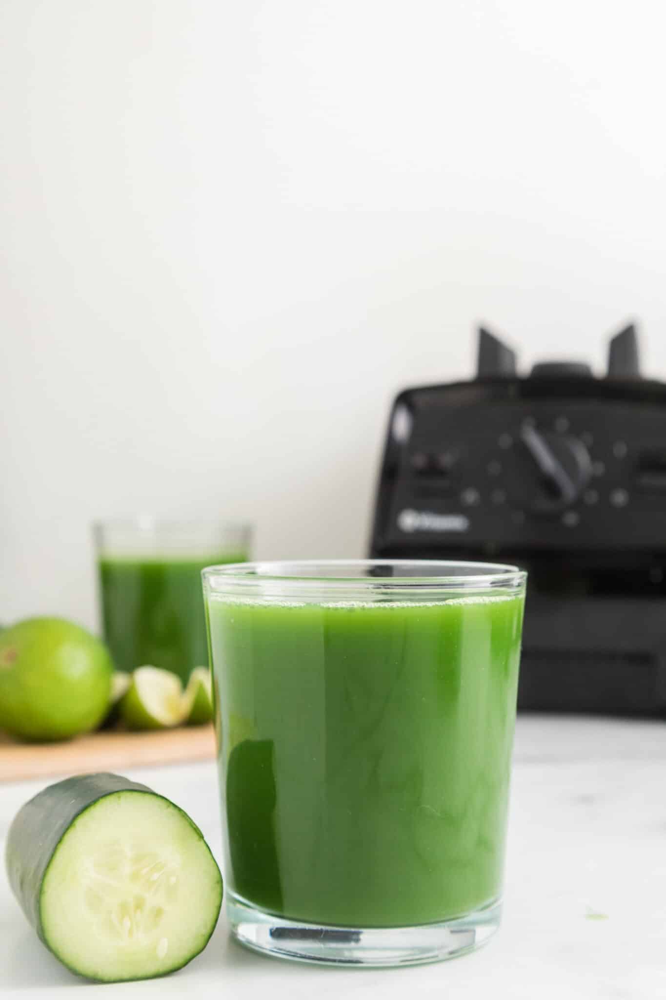 glass of cucumber juice on countertop with blender in background.