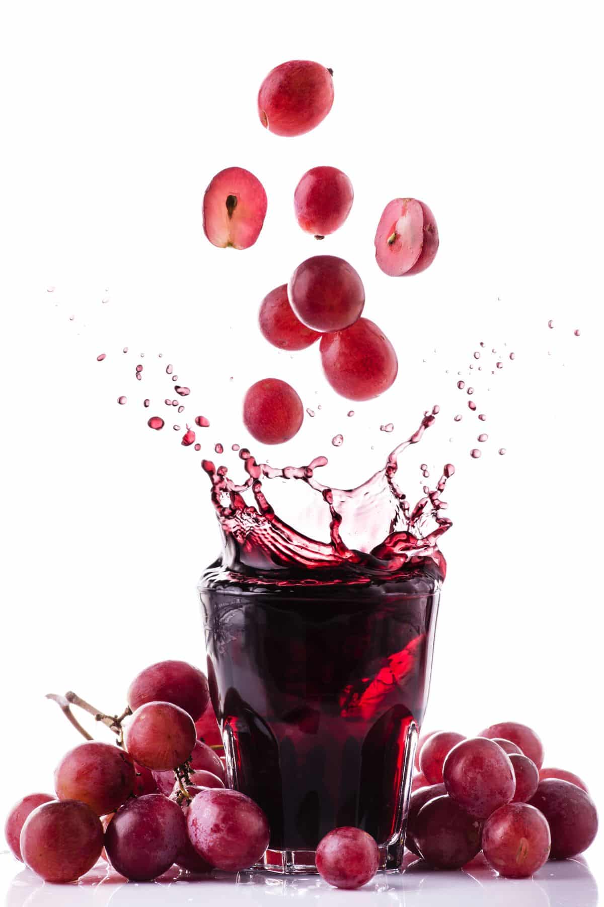 grapes falling into a glass of grape juice.