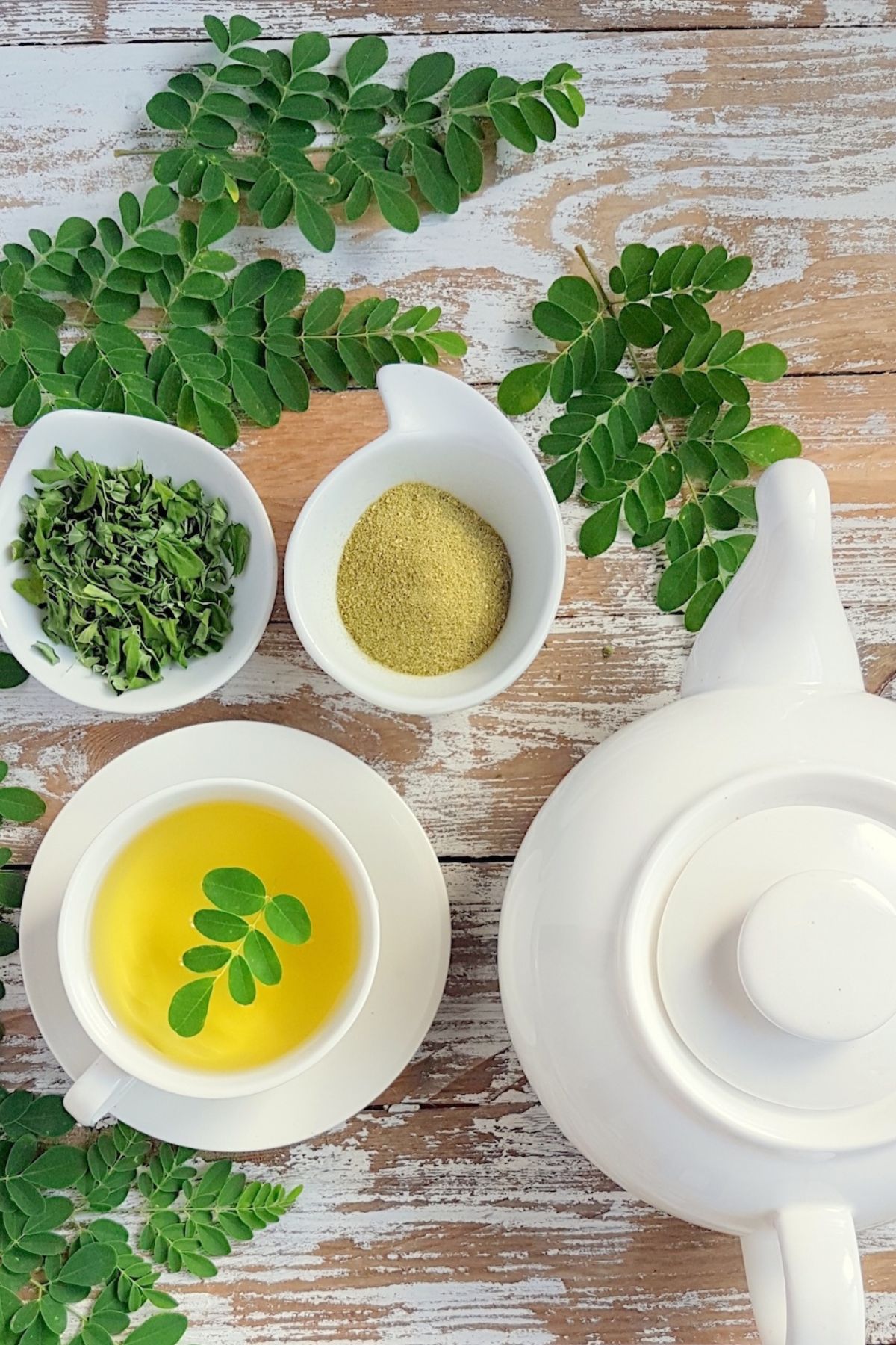 a mug of Moringa Tea next to a cup of moringa powder and a cup of moringa leaves.