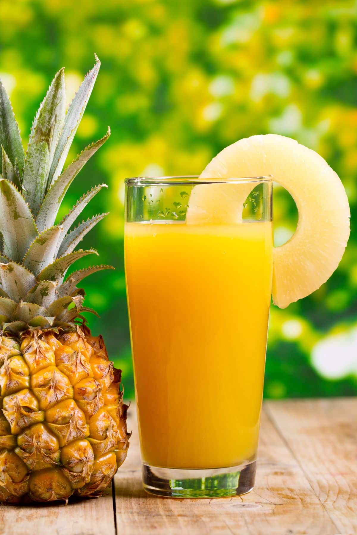 a glass of pineapple juice next to a whole pineapple.
