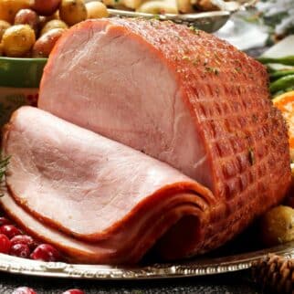 sliced ham on a table with vegetables in the background.
