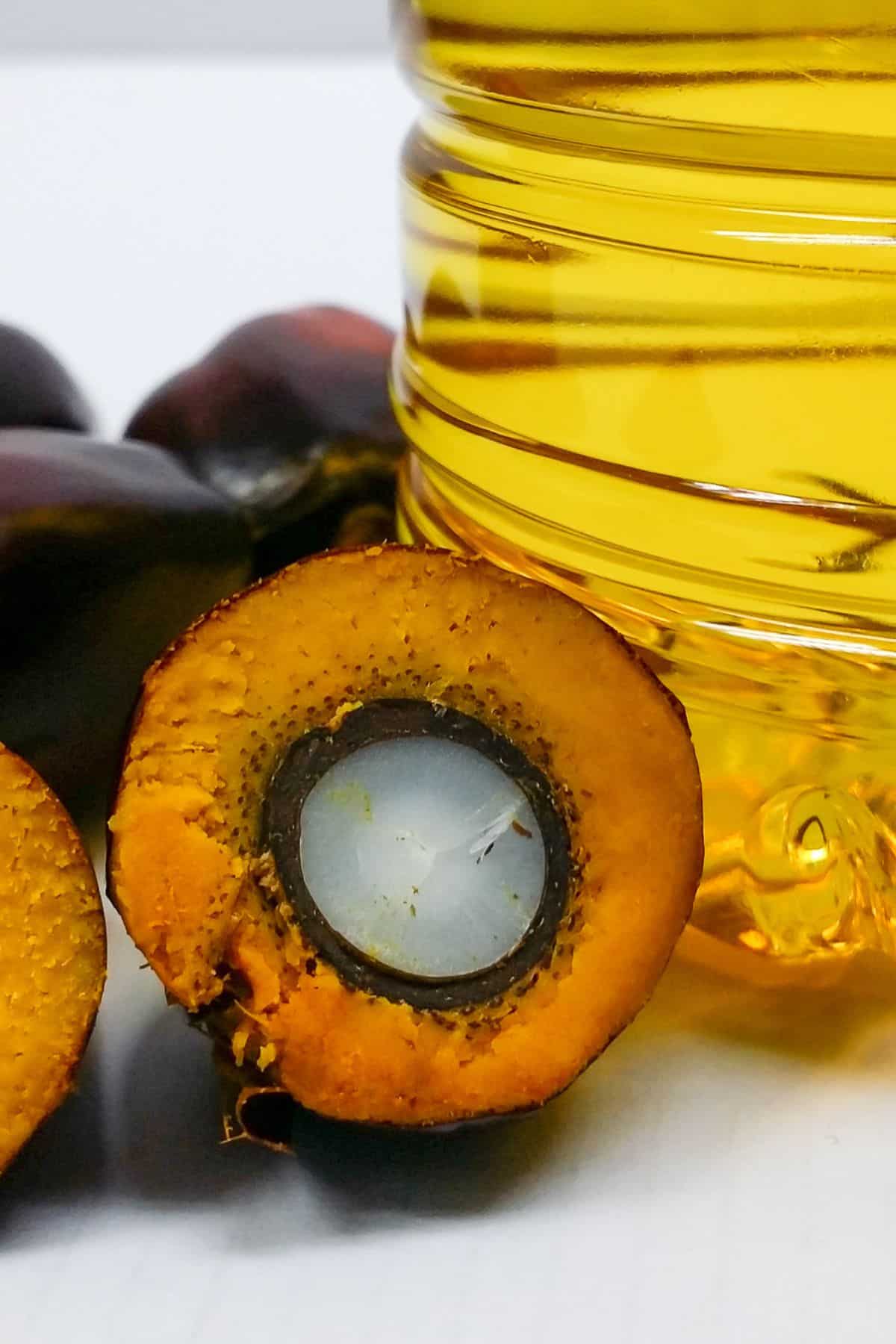 a palm fruit cut in half to show the kernel next to a jar of oil.