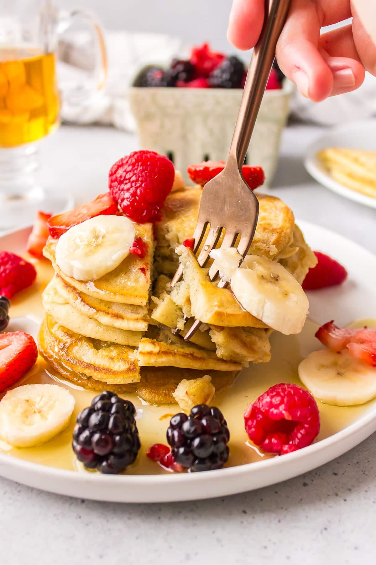 a fork holding a bite of pancakes topped with syrup and fruit.