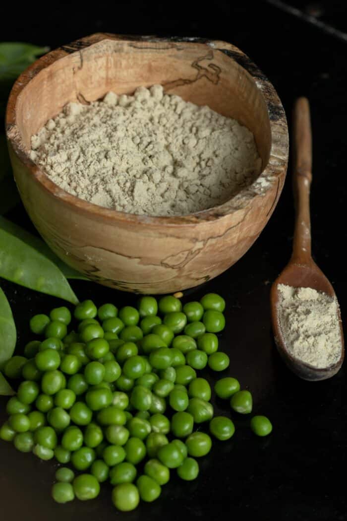 a bowl of pea protein powder next to peas on a black background.