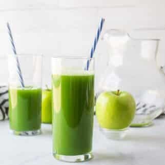 two glasses of green juice on table with straws.